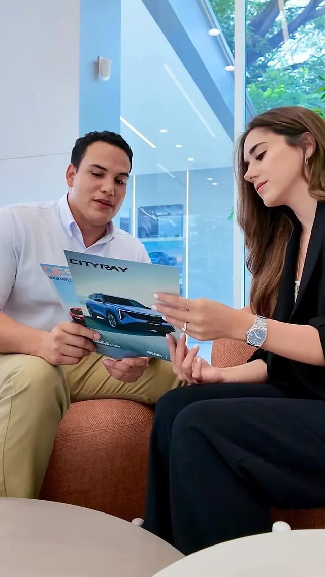 Dos personas revisan el folleto de un Geely en una sala de exhibición